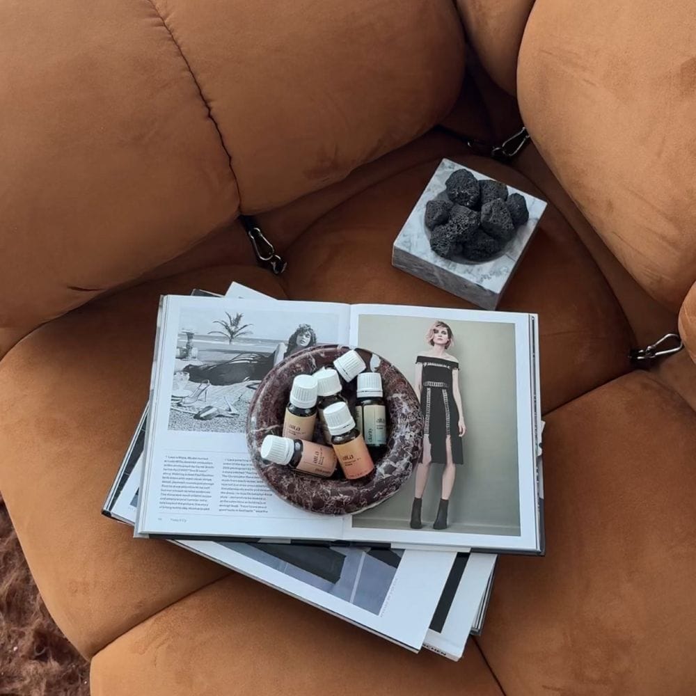Open magazine on a brown leather couch with oil bottles and lava stone diffuser